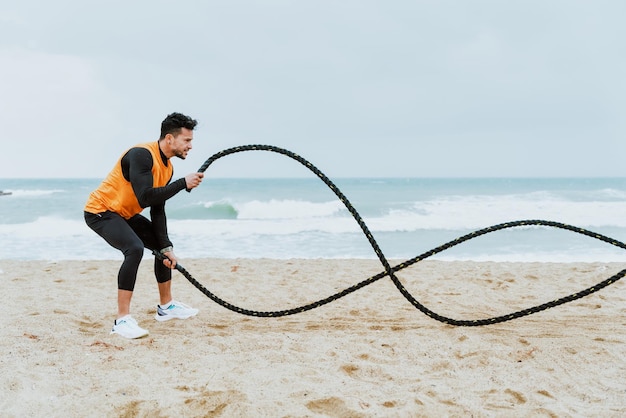 Young athlete training in the morning on the beach with\
ropes