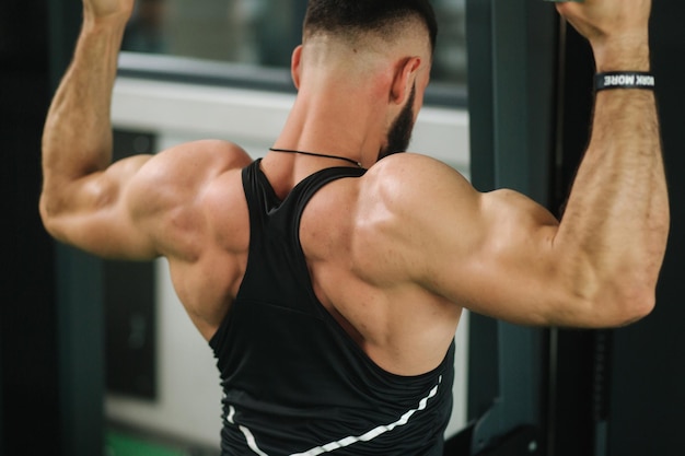 A young athlete trains in the gym Shows the muscles of the back and chest Back view