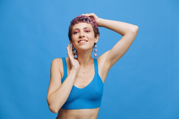 Young athletic fashion woman with colored hair and short haircut posing and dancing in blue sportswear smiling and looking at the camera on a blue monochrome background high quality photo