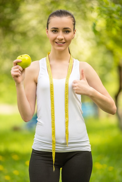 Молодая спортивная (ый) девушка ест зеленое яблоко после тренировки.