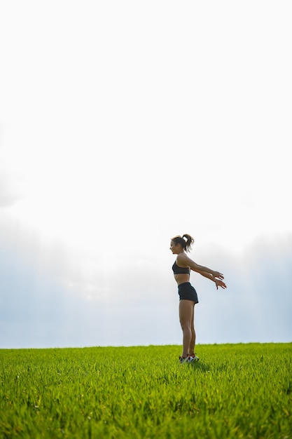 Young athletic girl makes jumping on the grass before sunset. Exercise, sports, healthy lifestyle