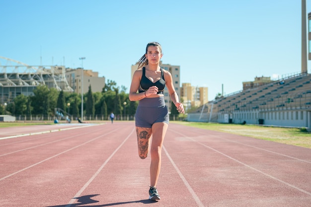 Young athletic girl with tattoos runs around a running track