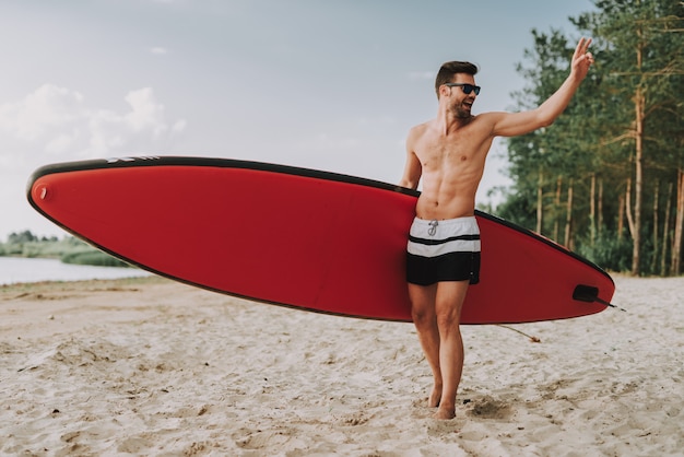 Photo young athletic guy with surf standing on beach.