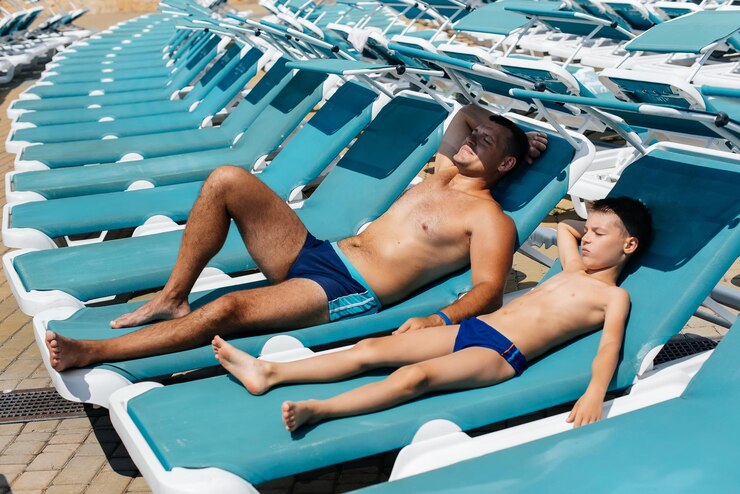 A young athletic man and his son are smiling happily and sunbathing on a sun lounger on a sunny day at the hotel Happy family vacation at a hotel in the resort Summer holidays and tourism