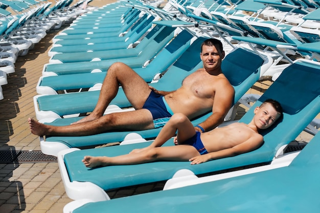 A young athletic man and his son are smiling happily and sunbathing on a sun lounger on a sunny day at the hotel Happy family vacation at a hotel in the resort Summer holidays and tourism