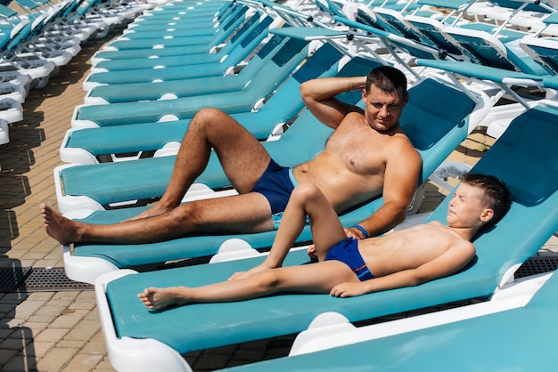 A young athletic man and his son are smiling happily and sunbathing on a sun lounger on a sunny day at the hotel Happy family vacation at a hotel in the resort Summer holidays and tourism