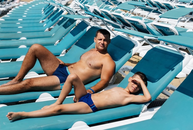 A young athletic man and his son are smiling happily and sunbathing on a sun lounger on a sunny day at the hotel Happy family vacation at a hotel in the resort Summer holidays and tourism