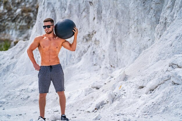 Young athletic man is holding medicine ball on the beach