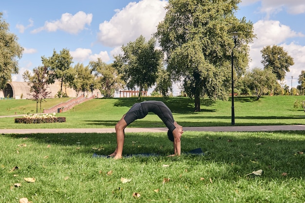 Young athletic man in sportswear doing yoga in the park