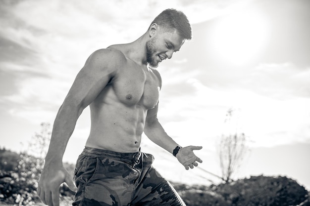 Young athletic man standing on the rock Bodybuilder with naked torso and wearing camouflage pants Healthy and beautiful body in black and white colours