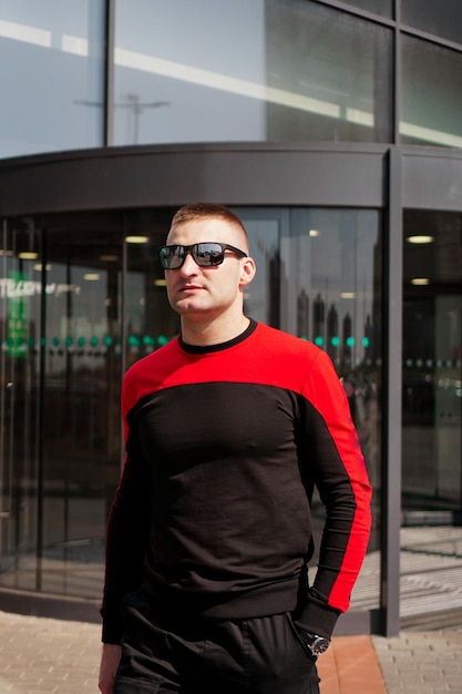 A young athletic man in sunglasses in a tracksuit walks out of the revolving doors of a hotel or shopping mall