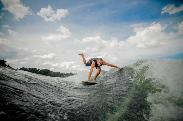 하늘을 강 아래로 보드에 젊고 운동 남자 wakesurfing