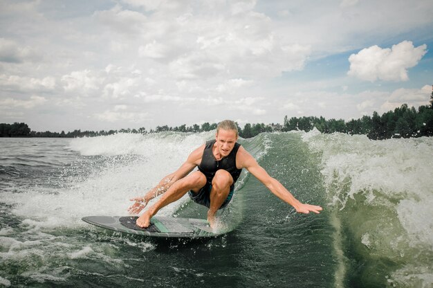 Young and athletic man wakesurfing on the board down the river