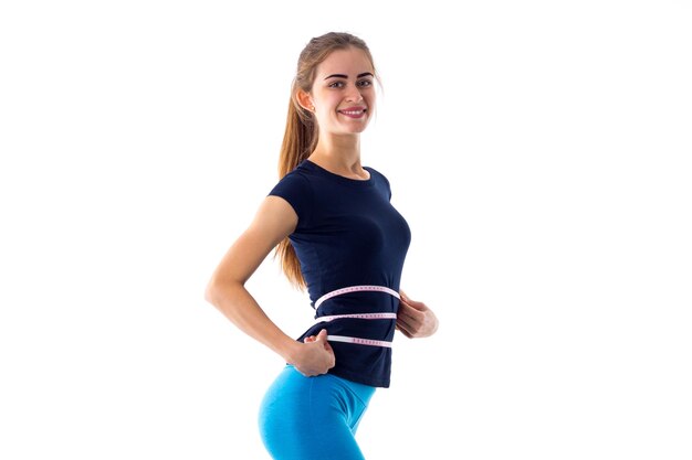 Young athletic woman in blue Tshirt and leggings measuring her buttocks with centimeter in studio
