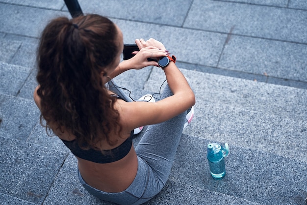 Young athletic woman checking her training results on sport watch while resting on stairs