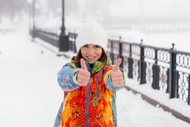 冷たい雪の日にスポーツをする若い運動女性が親指を立てます。フィットネス、ランニング