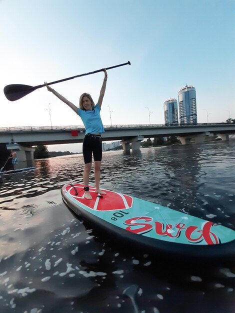 Молодая спортивная женщина плывет на весле SUP и подняла весло над собой для приветствия.