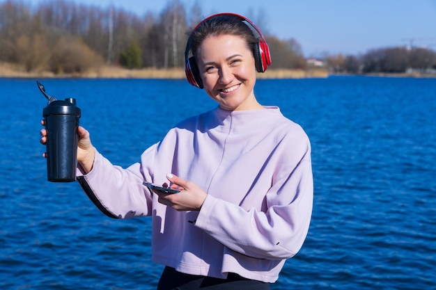 A young athletic woman listens to music and drinks water