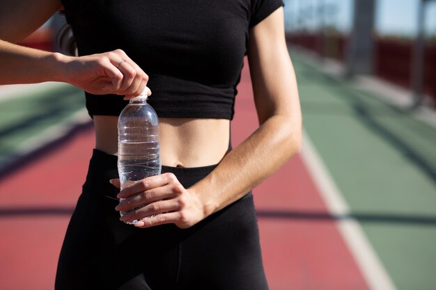 Молодая спортивная (ый) женщина открывая бутылку с водой во время бега на мосту. Место для текста