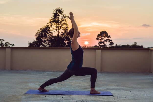 Young athletic woman practicing yoga on the roof at sunset, silhouette.