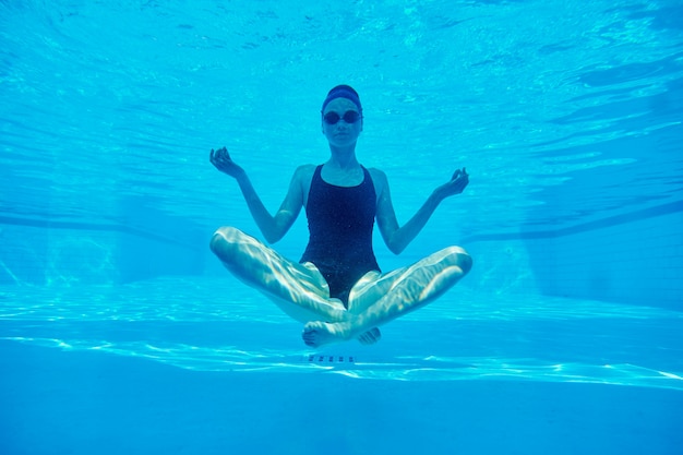 Foto giovane donna atletica che si siede nella posa del loto subacquea nella piscina