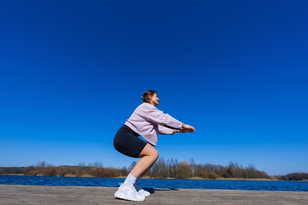 トレーニング中にしゃがむ運動選手の若い女性下から撮影ポイント池のビュー