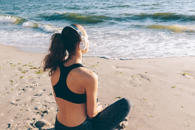 Young athletic woman with brown hair is sitting on the beach