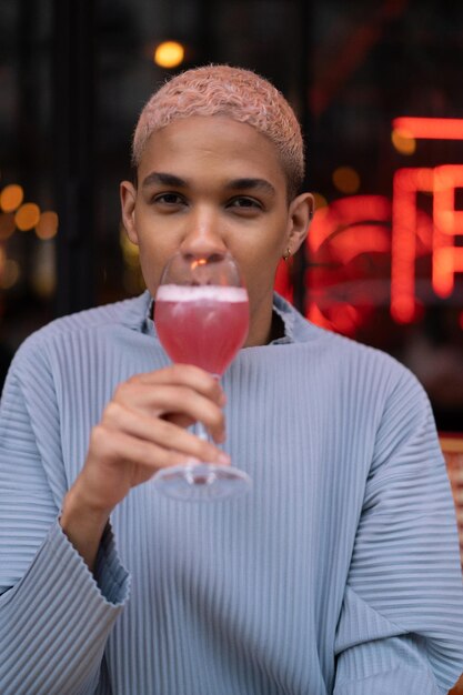 ピンクのコスモポリタンカクテル、ファッション撮影とカフェで若い魅力的なアフリカ系アメリカ人の男。パリ