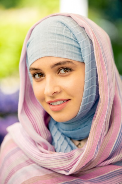 Young attractive Arabian female with natural makeup in hijab standing