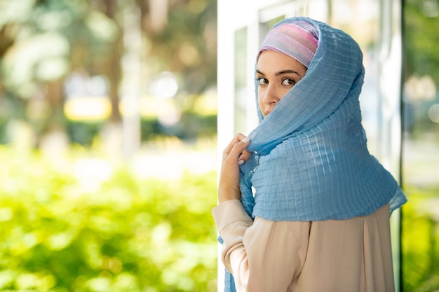 Young attractive Arabian woman in hijab looking at you over her shoulder in natural environment