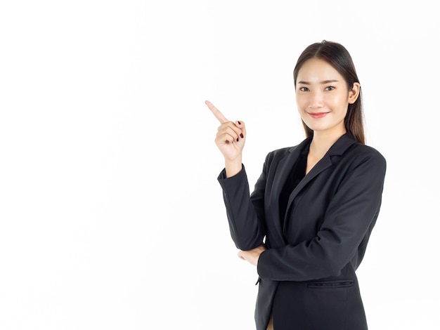 A young attractive Asian businesswoman in black suit pointing finger to present on copy space and looking camera.