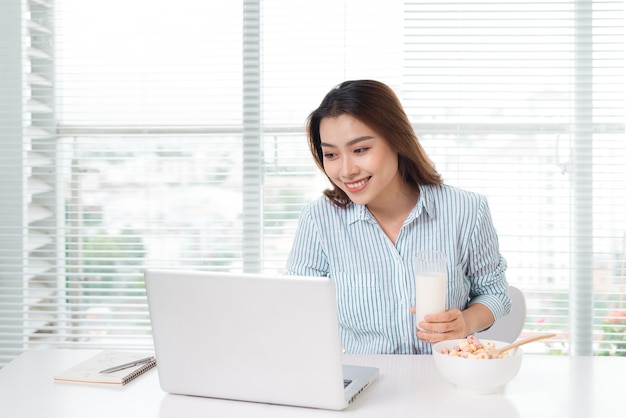 Young attractive asian businesswoman drinking milk while sitting at office desk