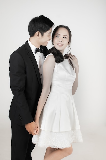 写真 若い魅力的なアジアのカップル、新郎新婦、白いウェディングドレスを着ている女性。一緒に立って、黒いタキシードを着ている男。結婚式前の写真撮影のコンセプト。