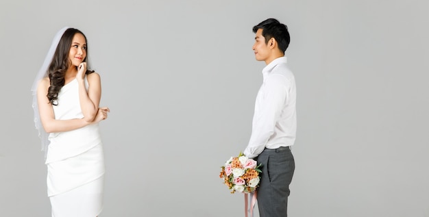 젊은 매력적인 아시아 커플, 흰색 셔츠를 입은 남자, 웨딩 베일이 떨어져 서 있는 흰색 드레스를 입은 여자. 꽃다발을 들고 있는 남자. 사전 결혼식 사진에 대한 개념입니다.