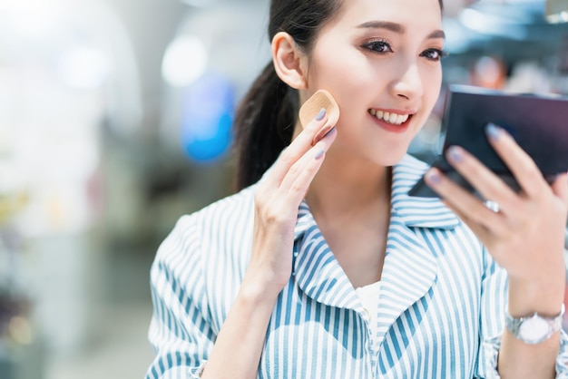 Young attractive asian female cheerful enjoy choosing cosmetics in shopping mall blur bokeh background