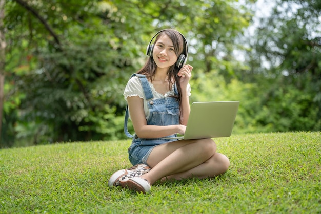 Young attractive asian female employee wear earphone listen to\
digital online course development study online in the park