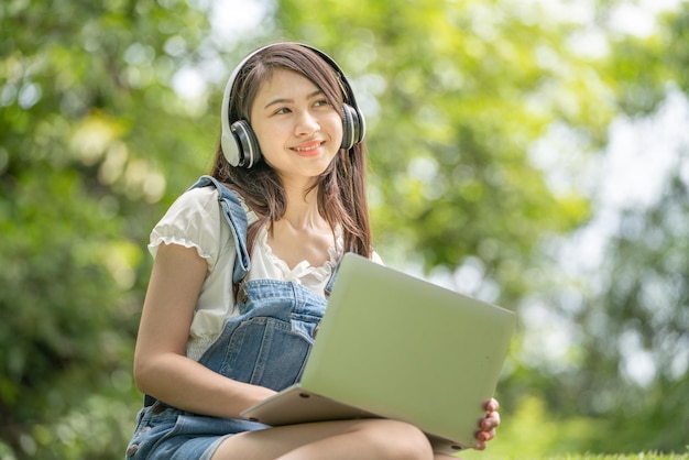 Young attractive asian female employee wear earphone listen to digital online course development study online in the park