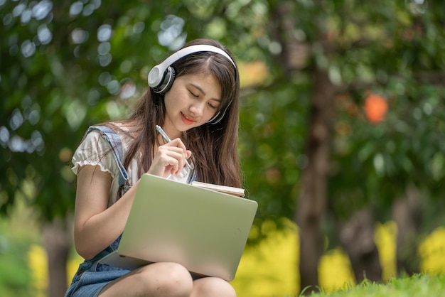 Young attractive asian female employee wear earphone listen to\
digital online course development study online in the park