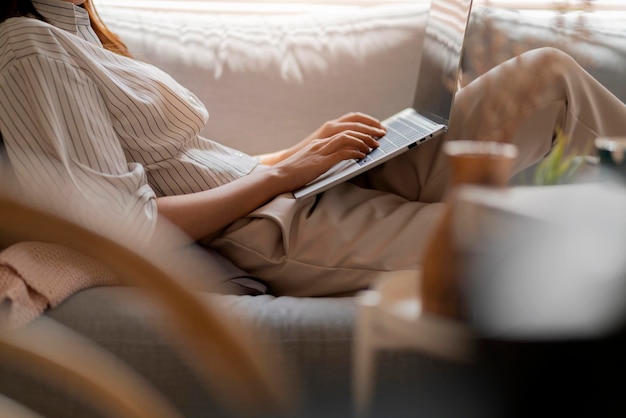 young attractive asian female working at home hand use laptop checking search schedule working process planning report with leisure relax on sofa in living room with morning light peaceful moment