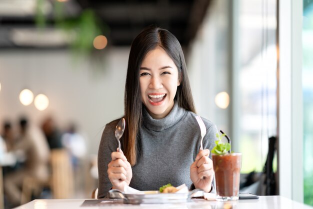 Photo young attractive asian woman holding fork and spoon