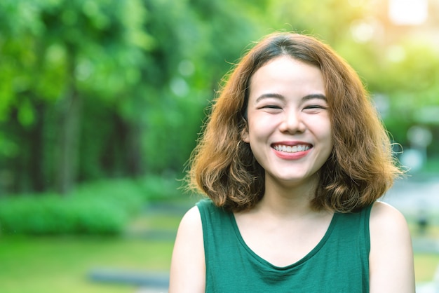 젊은 매력적인 아시아 여자 서, 너무 웃 고, 행복 하 고 집 또는 정원 배경 외부 자연 긍정적 인 카메라를보고. 아시아 아름다운 힙 스터 대학생.