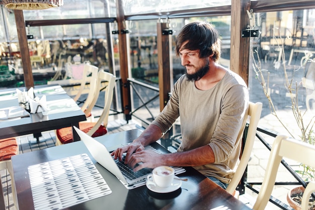 写真 屋外カフェでラップトップに入力する若い魅力的なひげを生やした男