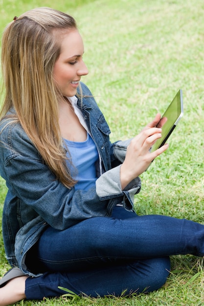 그녀의 태블릿 pc를 사용하는 동안 잔디에 앉아 젊은 매력적인 금발 소녀