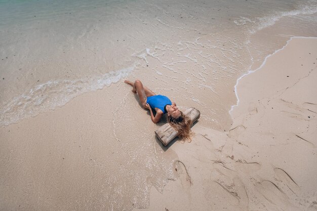 砂浜に横たわっている青い水着の若い魅力的なブロンドの女性。夏休みのコンセプト