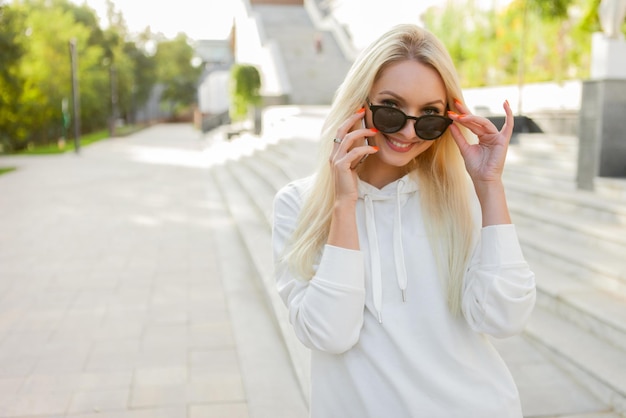 Фото Молодая привлекательная блондинка в солнечных очках разговаривает по телефону на улице