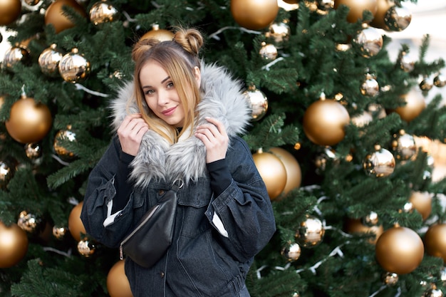 Young attractive blonde woman posing on the background of the christmas tree with golden balls.