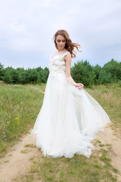 Young attractive bride with closed eyes in white stylish wedding dress outdoors, make up and hairstyle