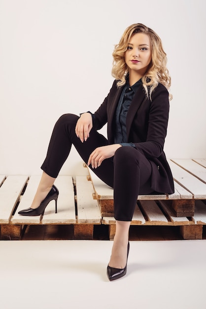 Young attractive business woman in expensive suit and shoes sits on painted pallets.