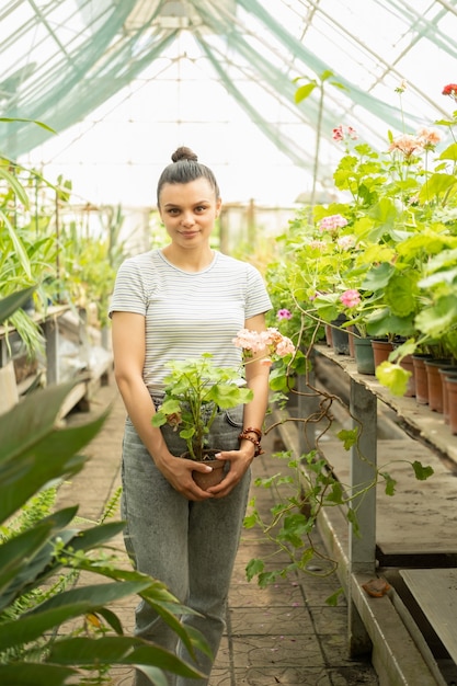 温室で花の植物とポットを保持しているカジュアルな服装で若い魅力的なビジネス女性。