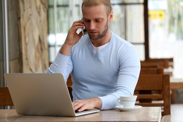 Young attractive businessman having lunch and working in a cafe